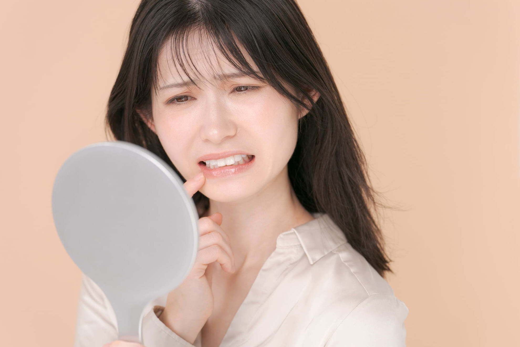 鏡を見て矯正治療後の歯が戻るのに気付いて驚く女性